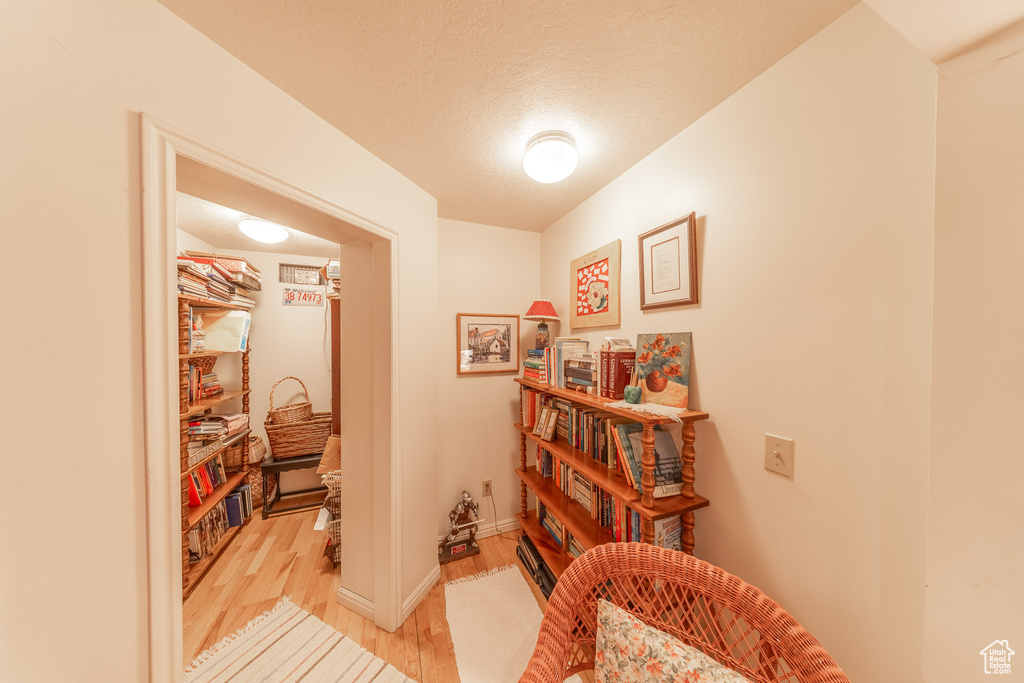 Hallway featuring light wood-style floors, baseboards, and a textured ceiling