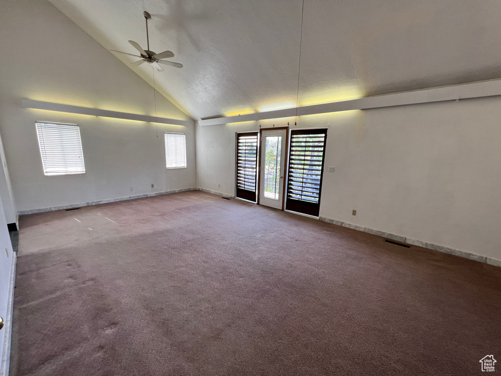 Carpeted empty room featuring ceiling fan, high vaulted ceiling, and baseboards