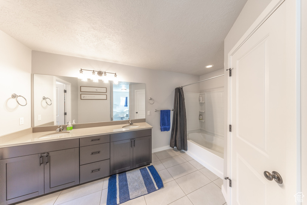 Full bathroom featuring tile patterned floors, double vanity, shower / bath combo with shower curtain, a textured ceiling, and baseboards