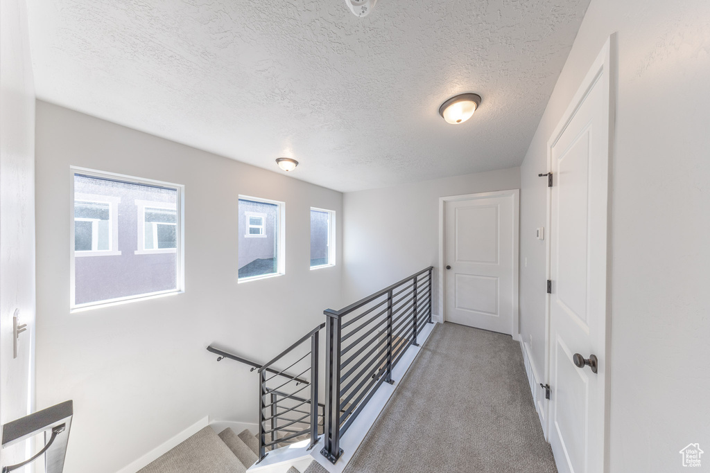 Corridor featuring an upstairs landing, carpet, a textured ceiling, and baseboards