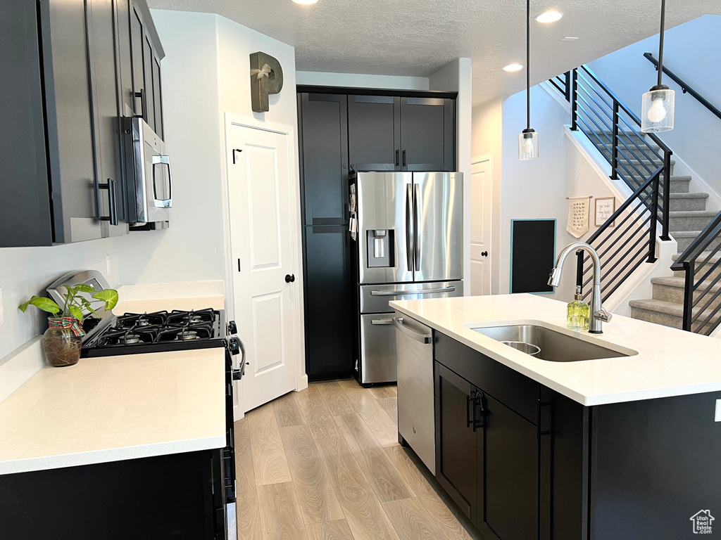 Kitchen with stainless steel appliances, light wood-type flooring, dark cabinetry, light countertops, and recessed lighting