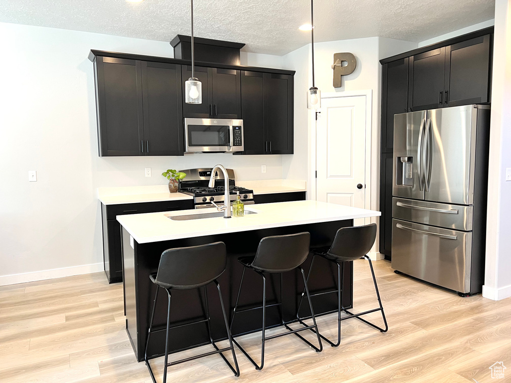 Kitchen with stainless steel appliances, dark cabinets, a textured ceiling, and hanging light fixtures