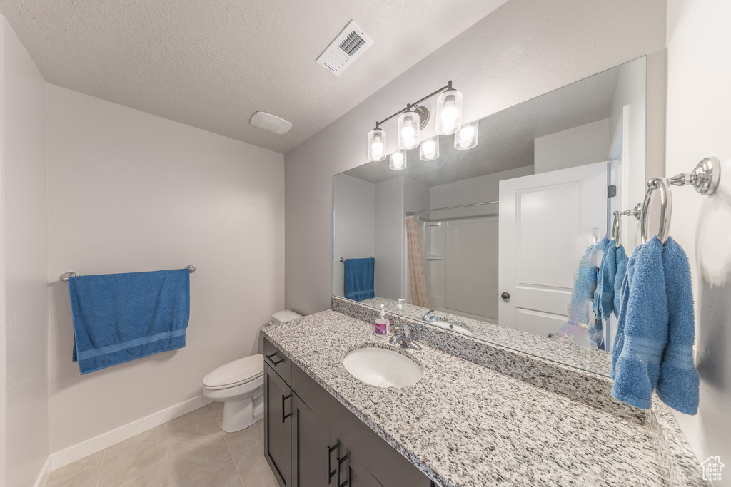 Bathroom featuring vanity, toilet, tile patterned flooring, baseboards, and a textured ceiling