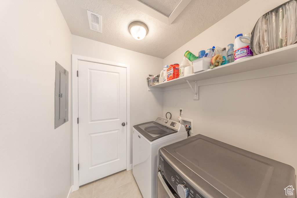 Laundry area with washer and clothes dryer, electric panel, light tile patterned floors, a textured ceiling, and baseboards