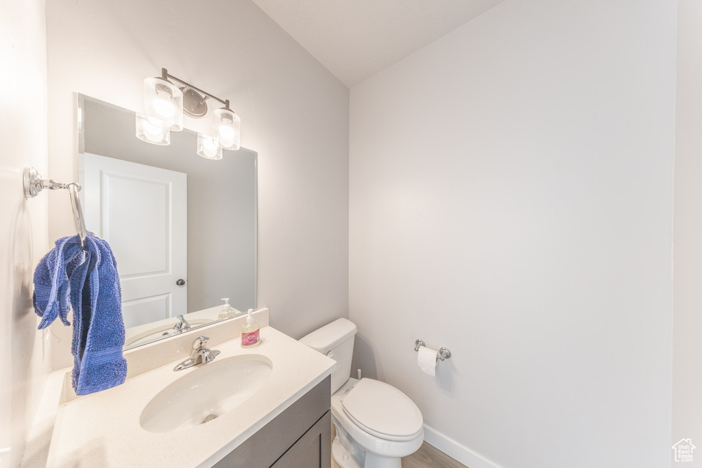 Bathroom featuring vanity, toilet, wood finished floors, and baseboards