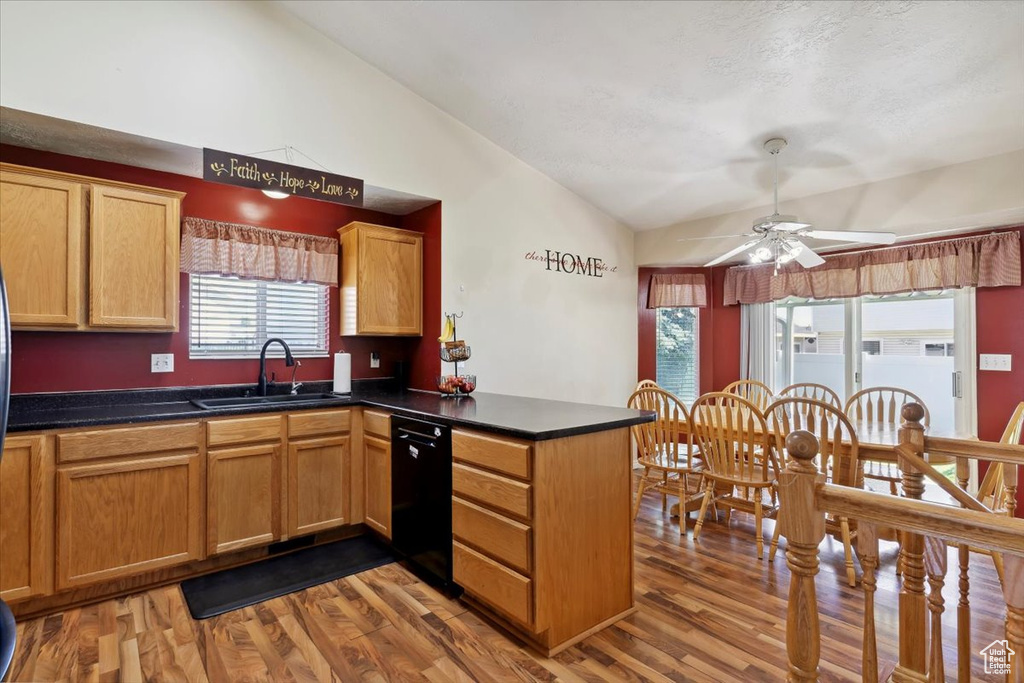Kitchen featuring dishwasher, vaulted ceiling, a sink, a peninsula, and wood finished floors