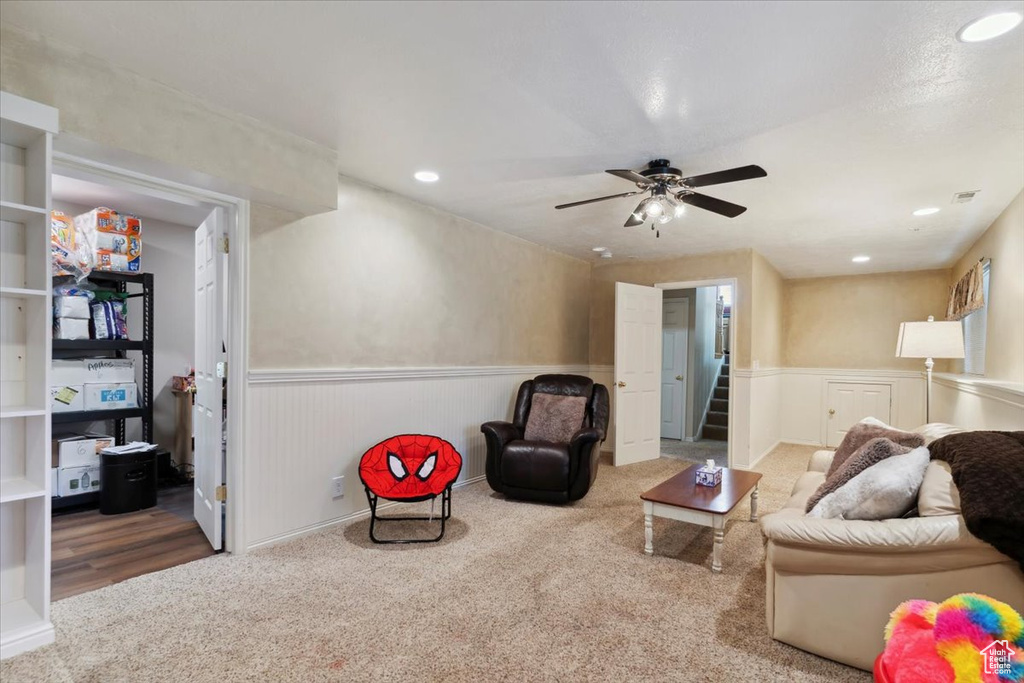 Carpeted living area with a wainscoted wall, stairway, ceiling fan, and recessed lighting