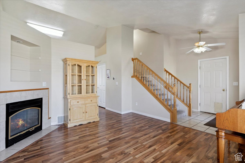 Unfurnished living room with wood finished floors, stairs, ceiling fan, a fireplace, and high vaulted ceiling