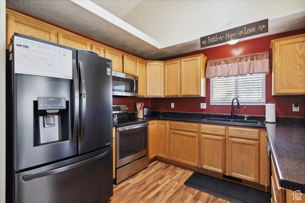 Kitchen featuring stainless steel appliances, a sink, light wood-style floors, and dark countertops