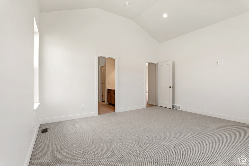 Unfurnished bedroom featuring light carpet, baseboards, high vaulted ceiling, and ensuite bathroom