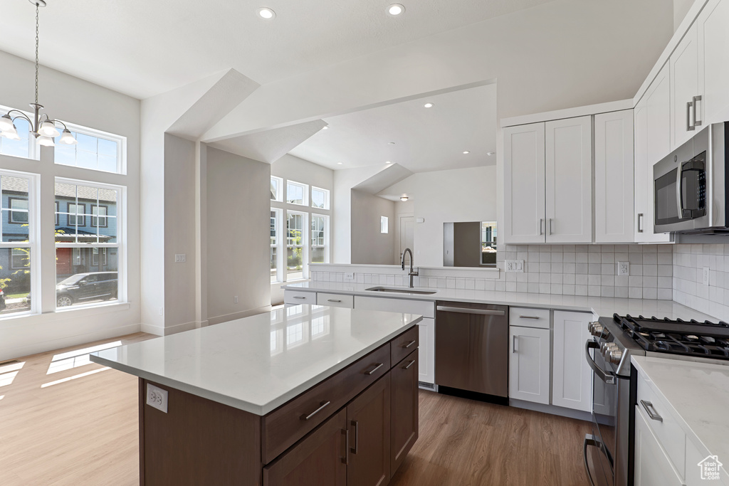 Kitchen with stainless steel appliances, a sink, light wood-style floors, light countertops, and decorative backsplash