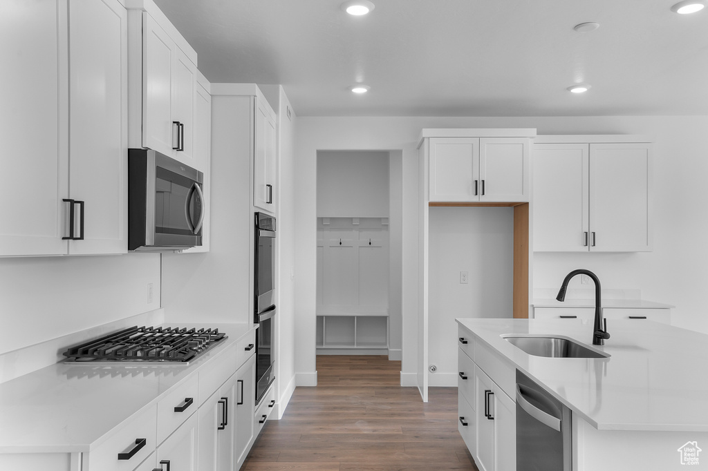 Kitchen featuring appliances with stainless steel finishes, a sink, recessed lighting, wood finished floors, and white cabinets