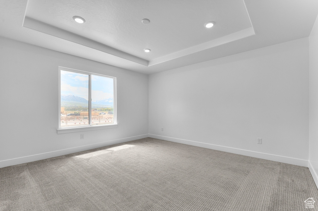 Carpeted empty room with a raised ceiling, baseboards, and recessed lighting