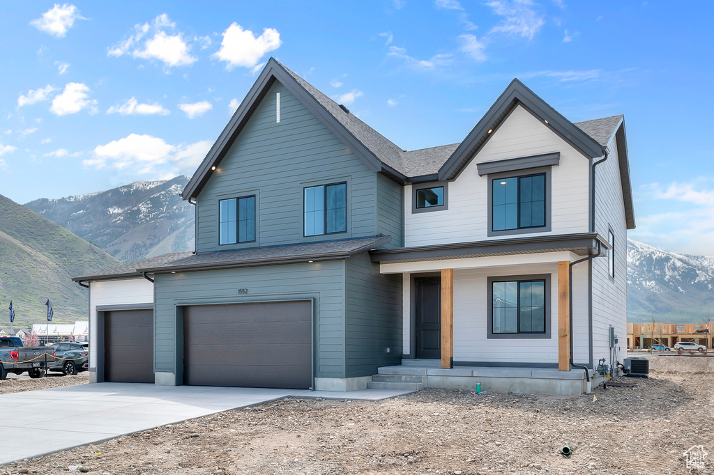 View of front of house featuring a mountain view, covered porch, concrete driveway, a garage, and central air condition unit