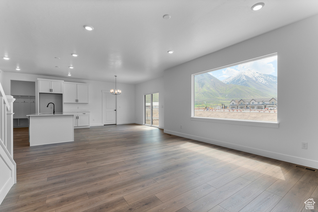 Unfurnished living room featuring a chandelier, recessed lighting, baseboards, dark wood-type flooring, and a mountain view