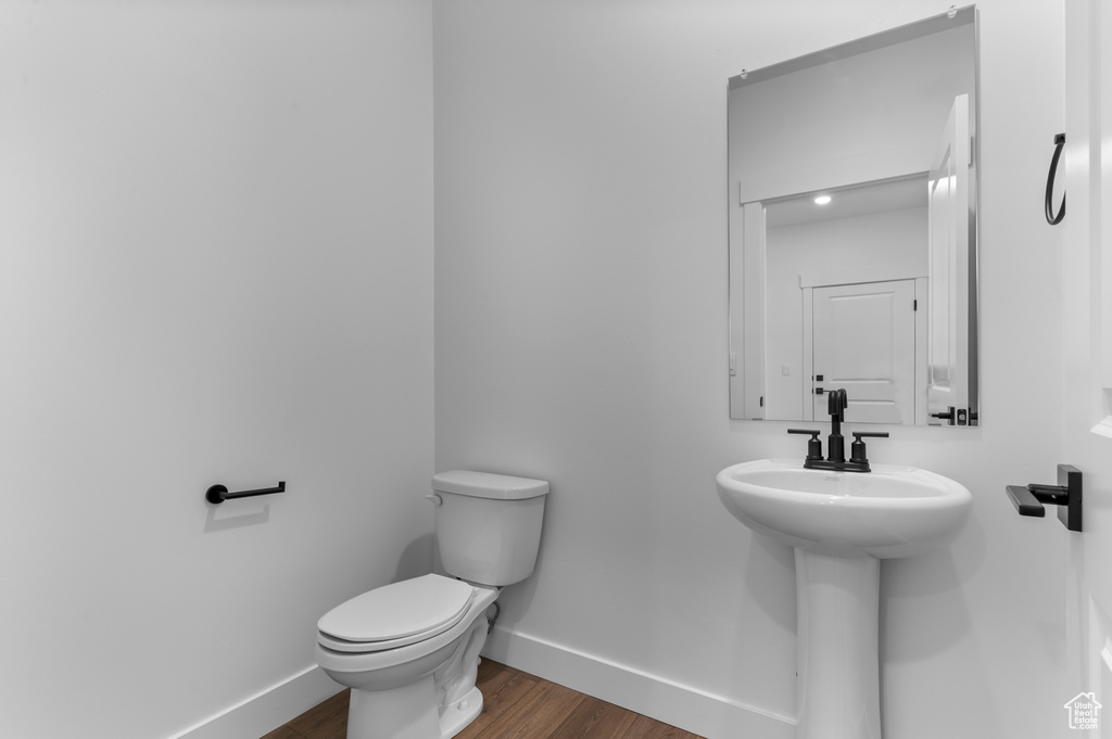 Half bath with baseboards, toilet, and wood finished floors