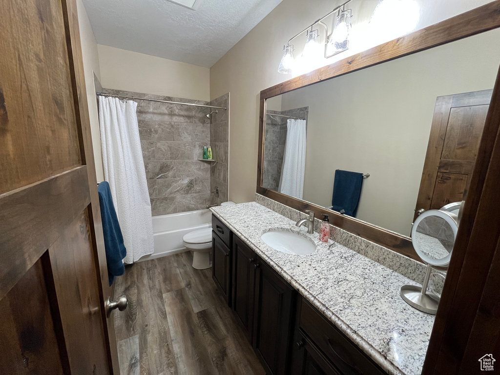 Full bathroom with double vanity, wood finished floors, shower / bath combination with curtain, toilet, and a textured ceiling