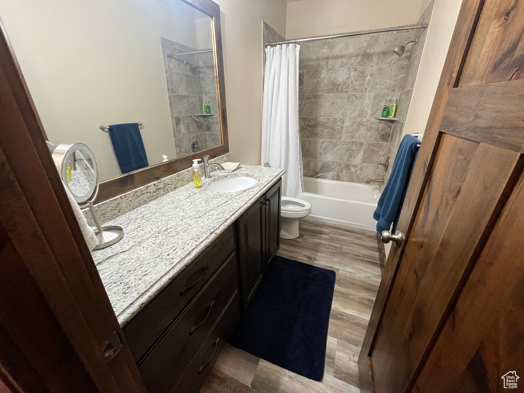 Bathroom featuring toilet, shower / tub combo, vanity, and wood finished floors