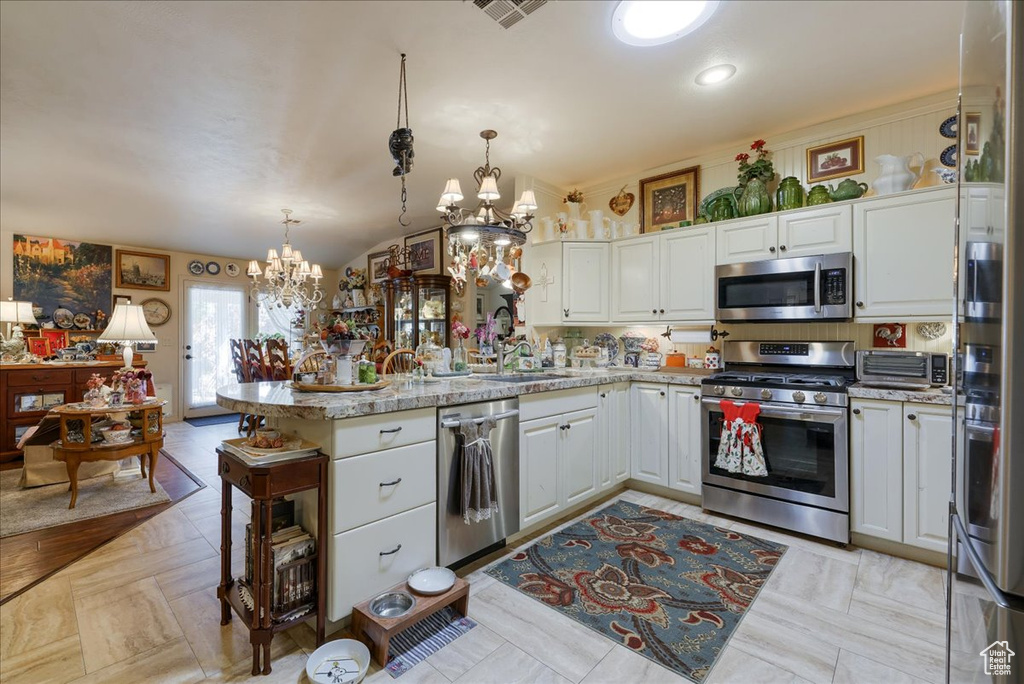 Kitchen featuring appliances with stainless steel finishes, a chandelier, a peninsula, white cabinetry, and a sink