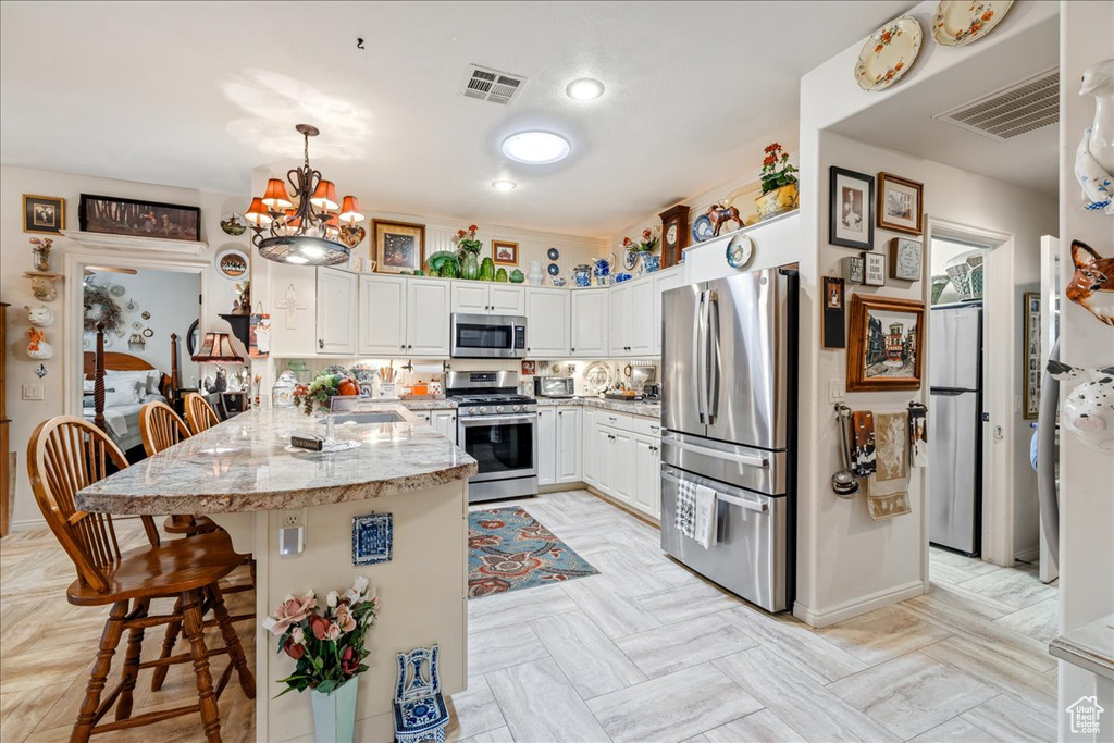 Kitchen featuring stainless steel appliances, a peninsula, a breakfast bar, a chandelier, and white cabinets