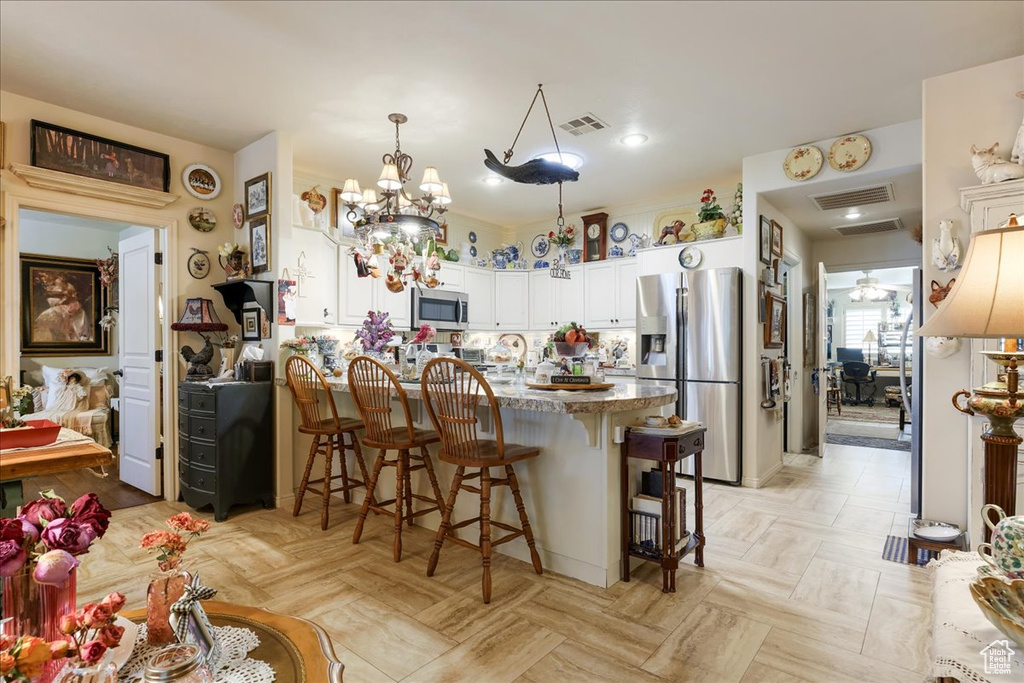 Kitchen featuring appliances with stainless steel finishes, a peninsula, a kitchen bar, light stone counters, and white cabinetry