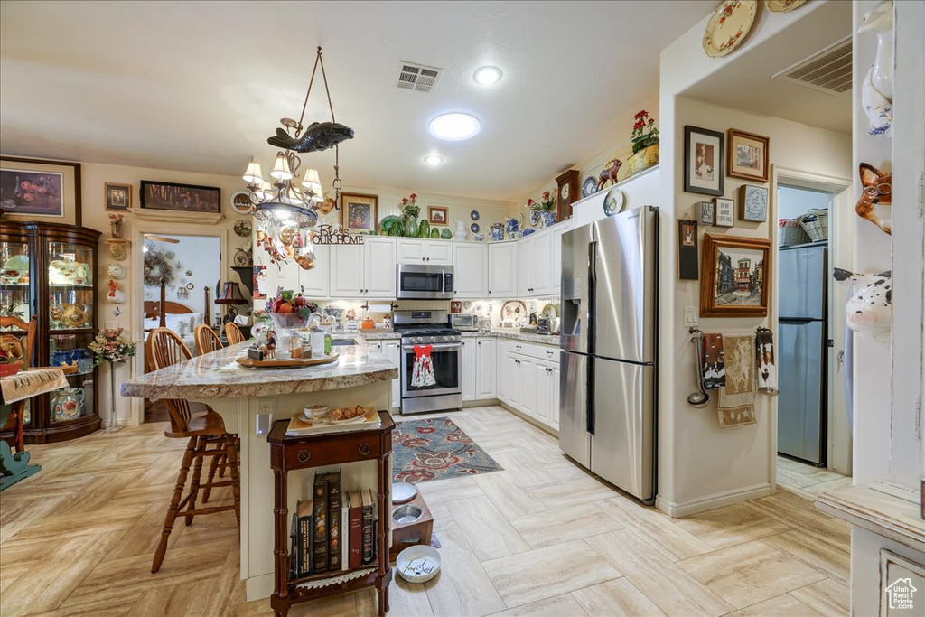 Kitchen featuring stainless steel appliances, white cabinets, light countertops, a breakfast bar area, and hanging light fixtures