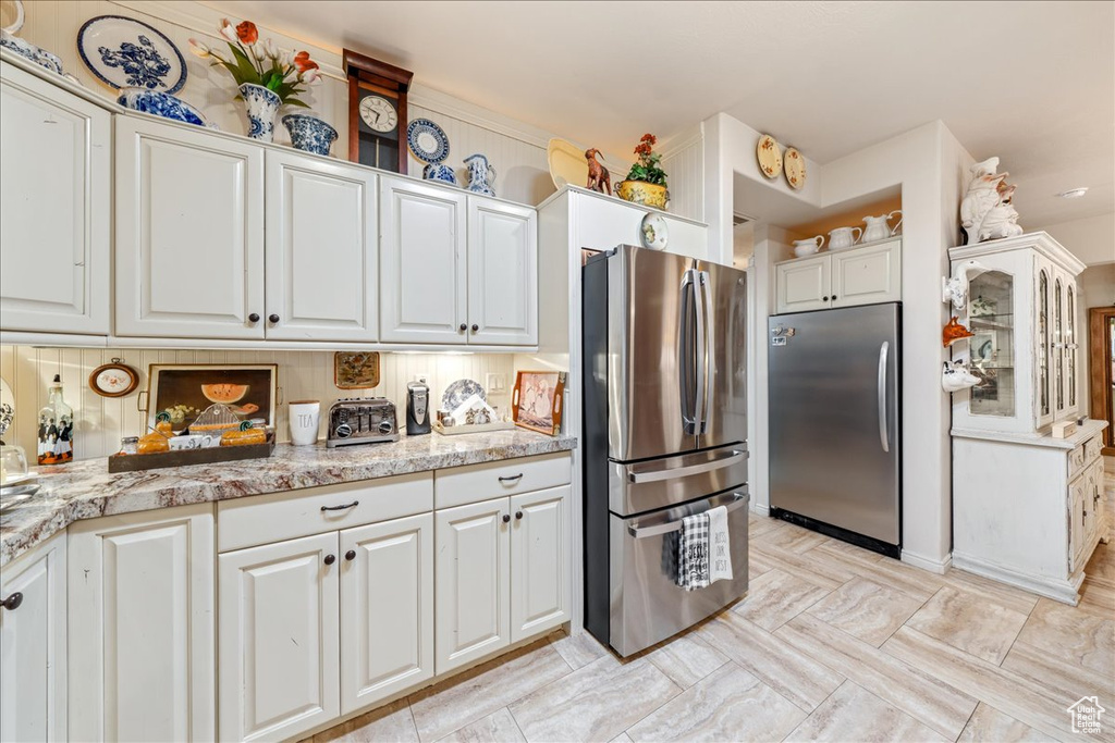 Kitchen featuring freestanding refrigerator, white cabinets, and light stone counters
