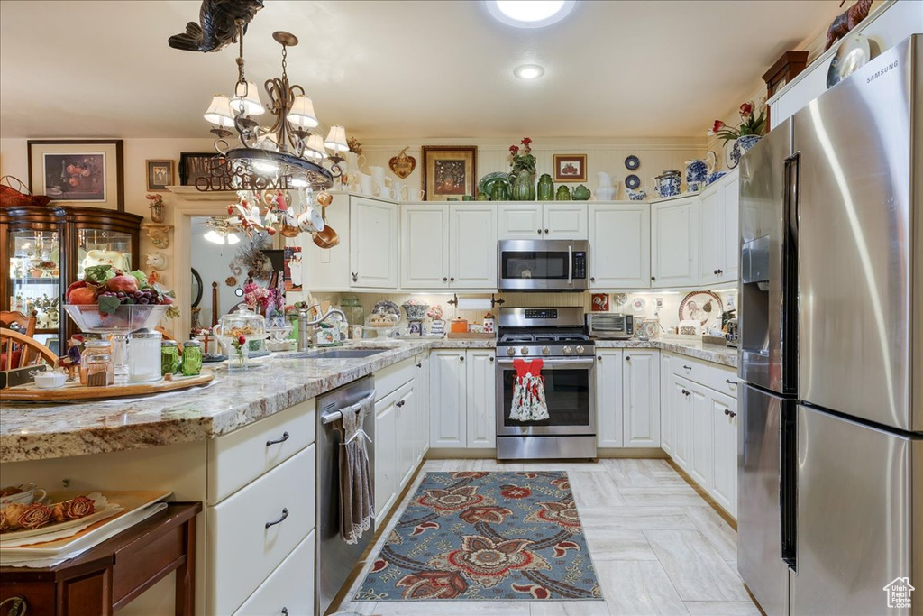 Kitchen with stainless steel appliances, white cabinets, a sink, and decorative light fixtures