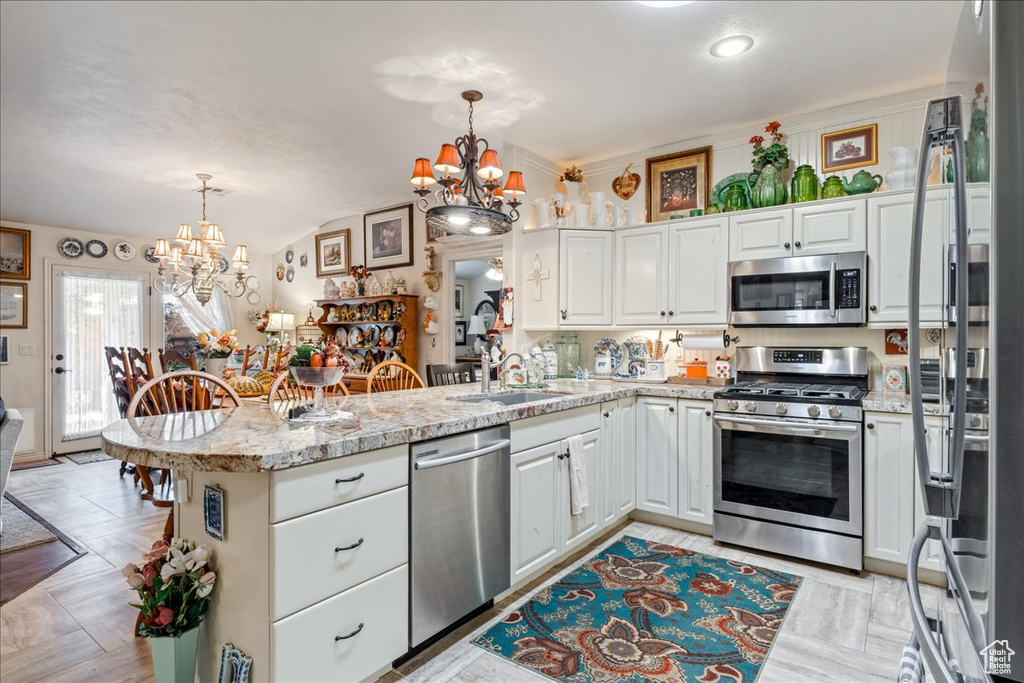 Kitchen with stainless steel appliances, a chandelier, a peninsula, white cabinets, and vaulted ceiling