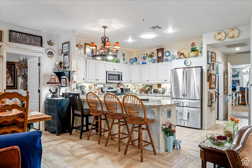Kitchen with stainless steel appliances, a peninsula, a chandelier, a breakfast bar area, and white cabinetry