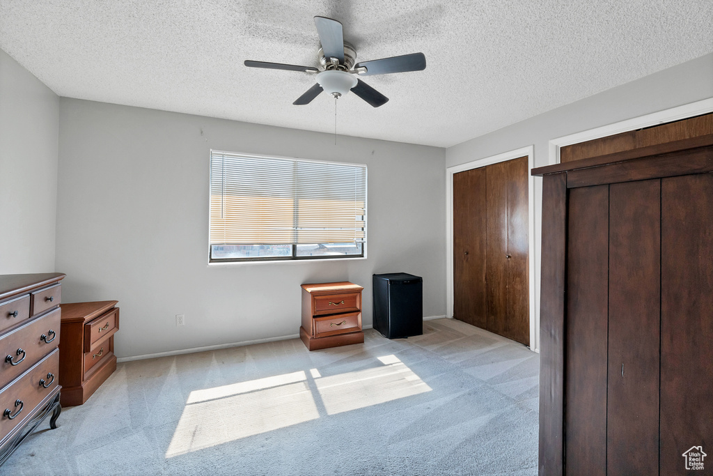 Unfurnished bedroom with light carpet, multiple closets, a textured ceiling, and ceiling fan