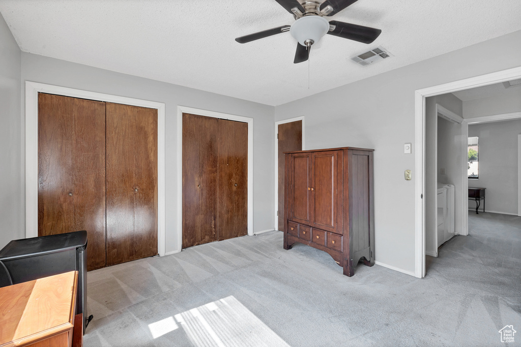 Bedroom with separate washer and dryer, light carpet, two closets, baseboards, and ceiling fan