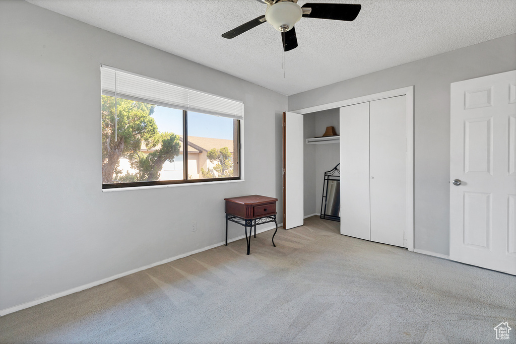 Unfurnished bedroom featuring light carpet, a textured ceiling, a closet, baseboards, and a ceiling fan