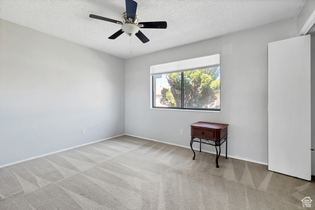 Carpeted empty room with a textured ceiling, ceiling fan, and baseboards