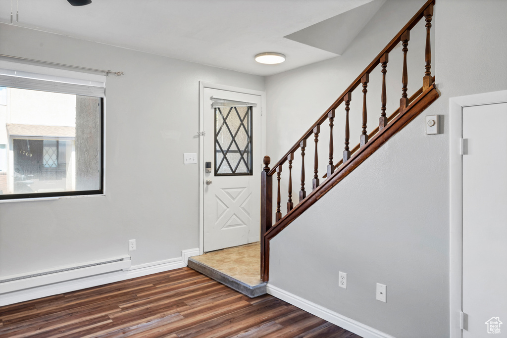 Foyer entrance with dark wood finished floors, a baseboard radiator, baseboards, and stairs