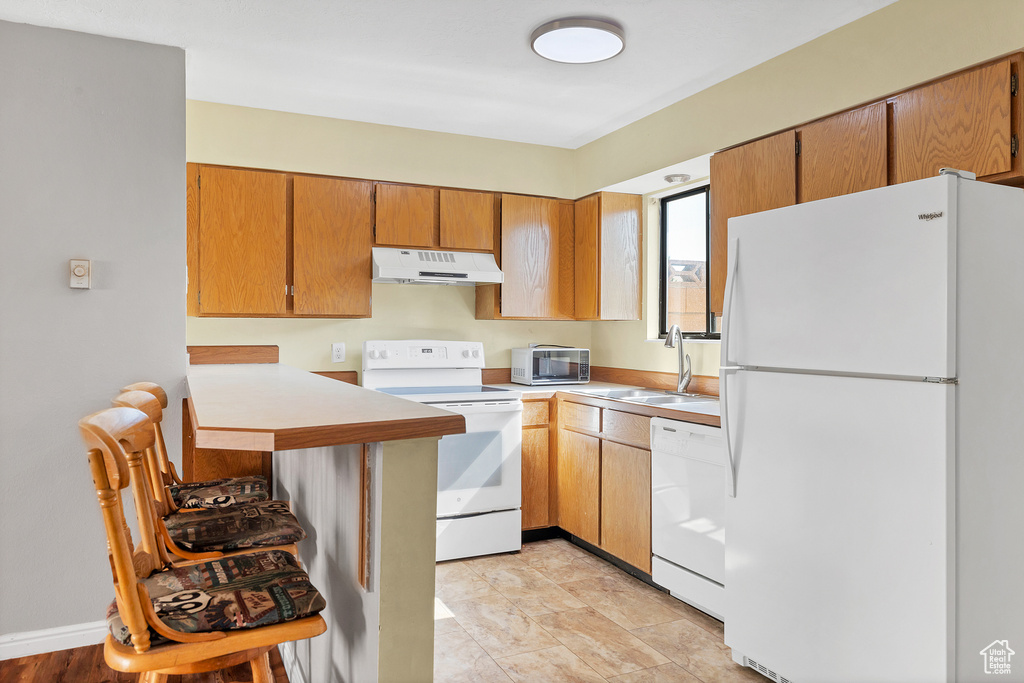 Kitchen featuring white appliances, under cabinet range hood, a sink, light countertops, and brown cabinets