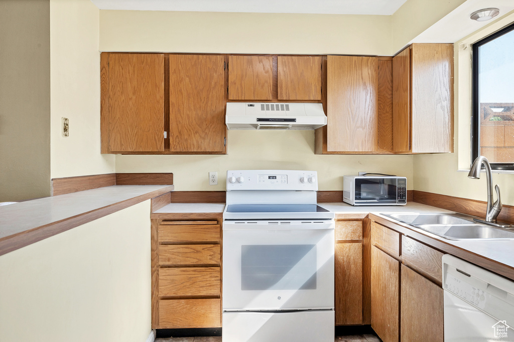Kitchen featuring under cabinet range hood, white appliances, a sink, light countertops, and brown cabinets