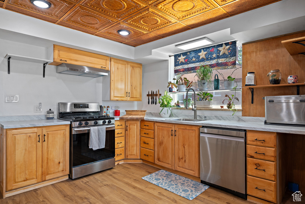 Kitchen featuring appliances with stainless steel finishes, open shelves, a sink, light wood-style flooring, and an ornate ceiling