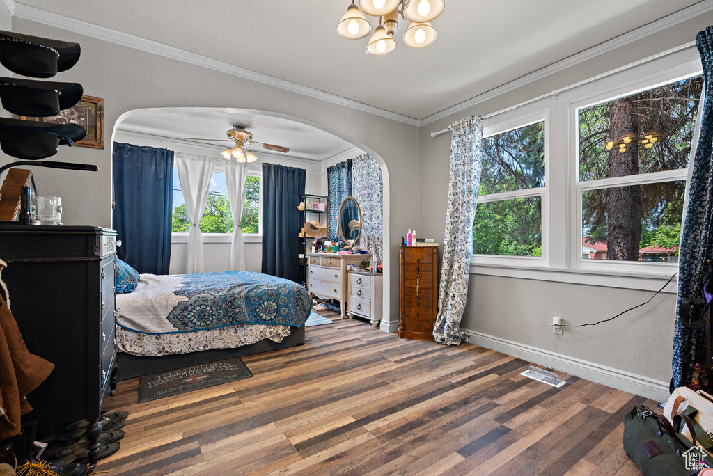 Bedroom with arched walkways, wood finished floors, ornamental molding, a chandelier, and baseboards