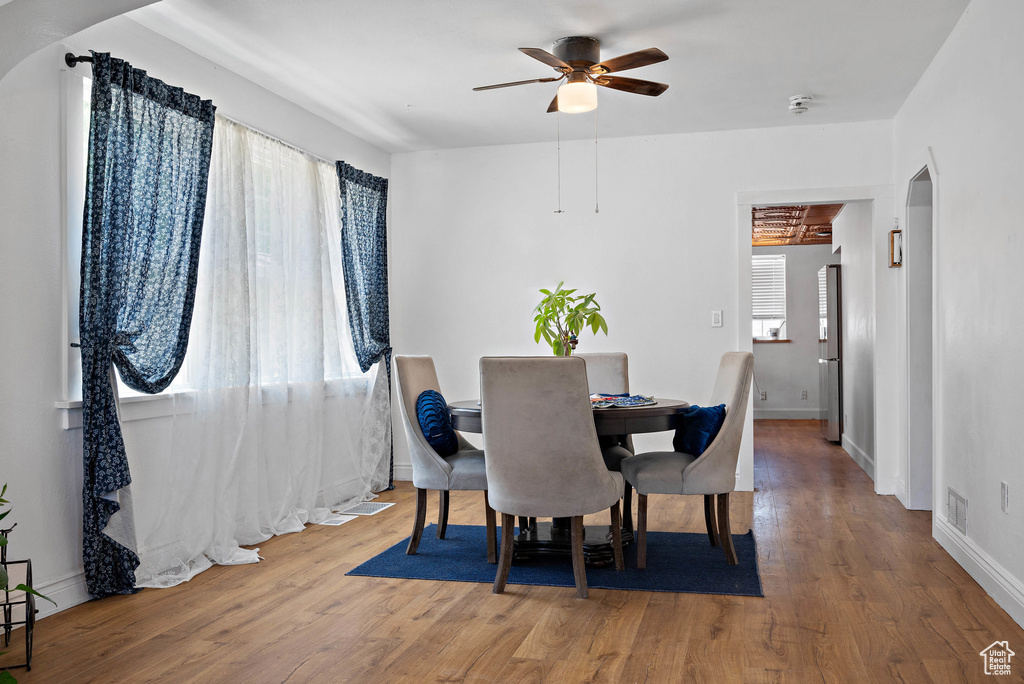 Dining space with a ceiling fan, arched walkways, and wood finished floors