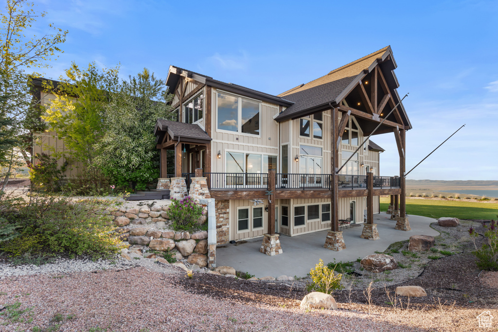 Back of property with a patio area, roof with shingles, and board and batten siding