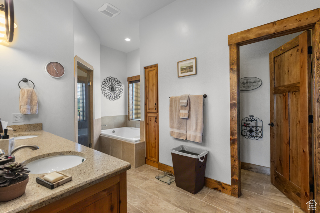 Full bathroom featuring double vanity, a garden tub, recessed lighting, and baseboards