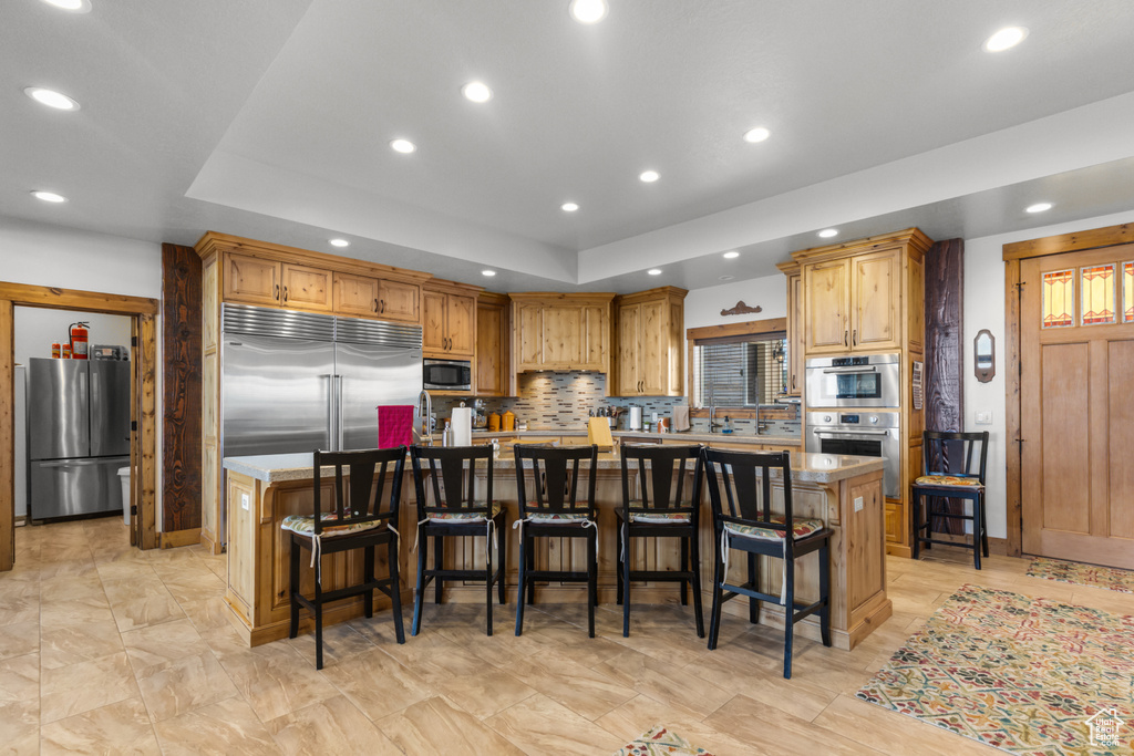 Kitchen with built in appliances, a large island, a raised ceiling, recessed lighting, and tasteful backsplash