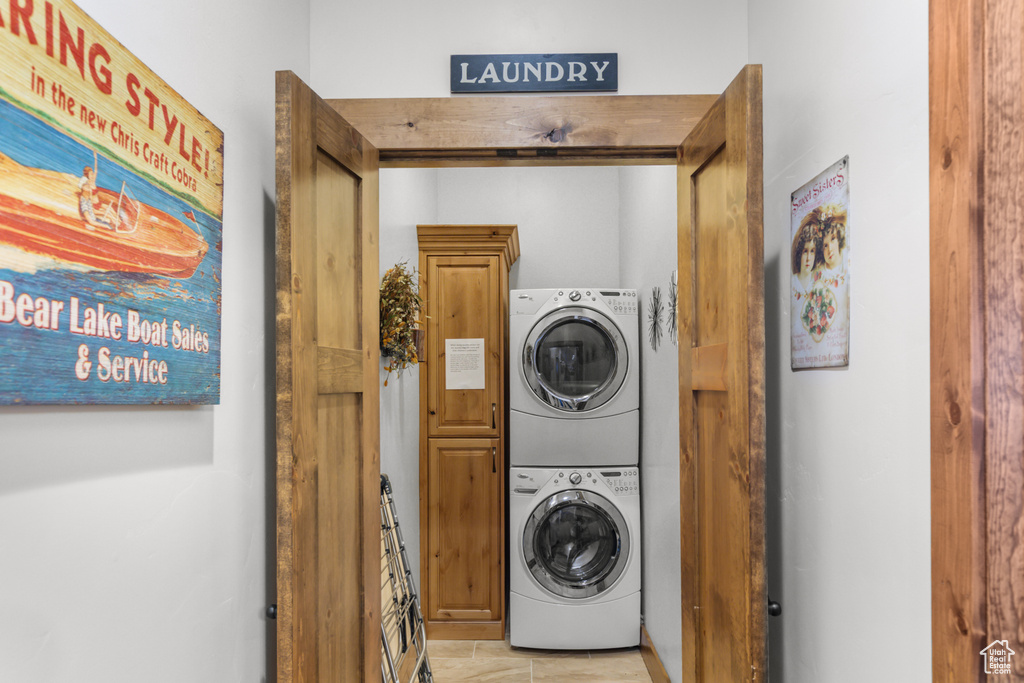 Laundry area with stacked washer / drying machine, light tile patterned floors, and cabinet space