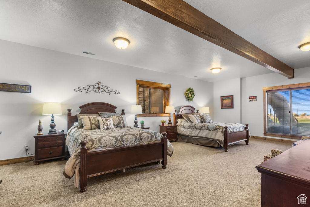 Bedroom featuring light carpet, beam ceiling, baseboards, and a textured ceiling