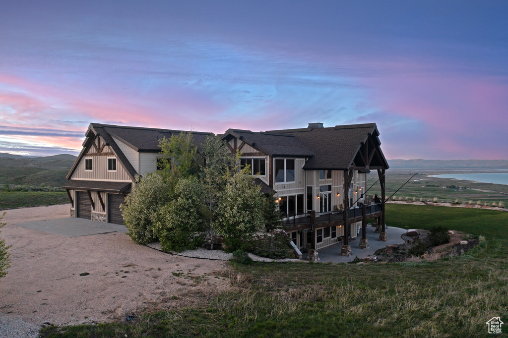 View of side of home with dirt driveway, an attached garage, board and batten siding, a water view, and a patio area