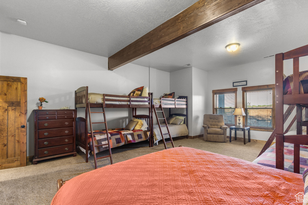 Bedroom featuring carpet floors, a textured ceiling, beam ceiling, and baseboards