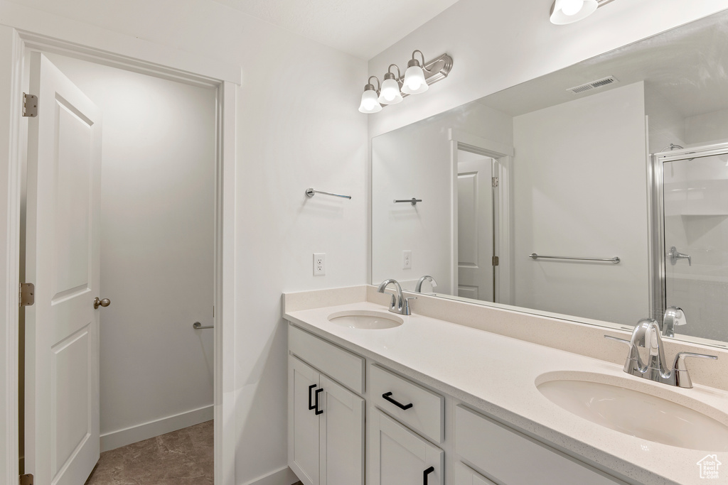 Full bathroom with double vanity, a shower with door, and baseboards