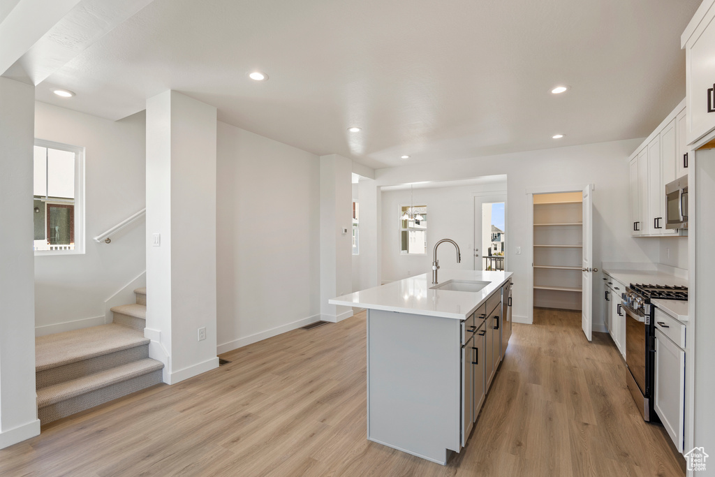 Kitchen with a sink, stainless steel appliances, light wood finished floors, a center island with sink, and recessed lighting