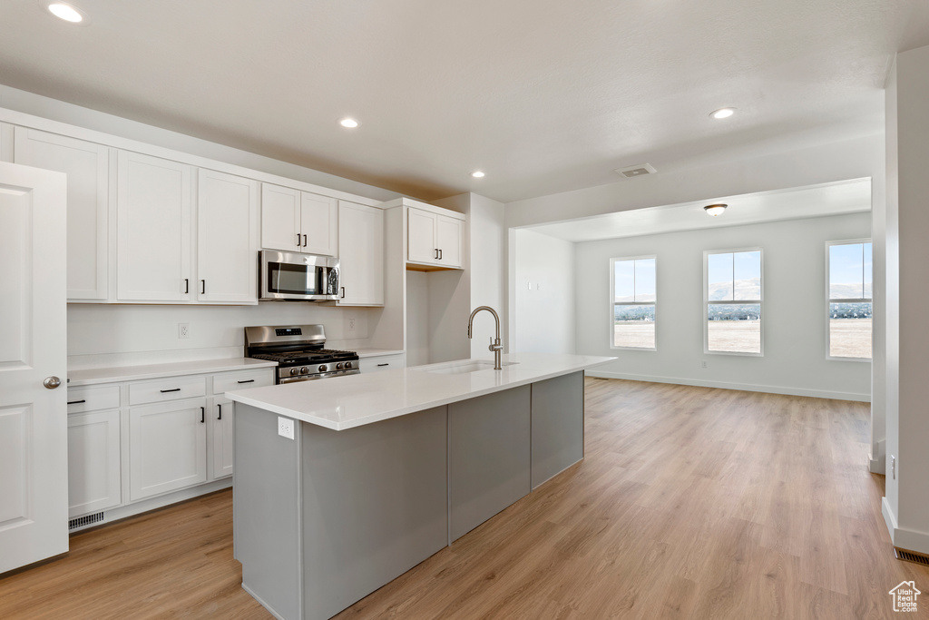 Kitchen with stainless steel appliances, a sink, light wood finished floors, light countertops, and white cabinetry